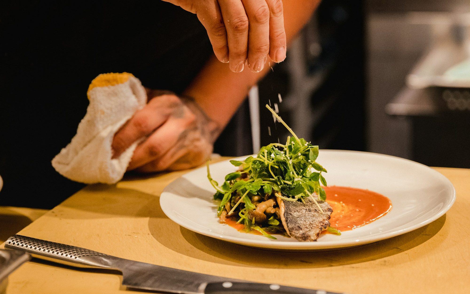 Chef Charlie Weintraub finishing a plate of seared fish with fresh greens