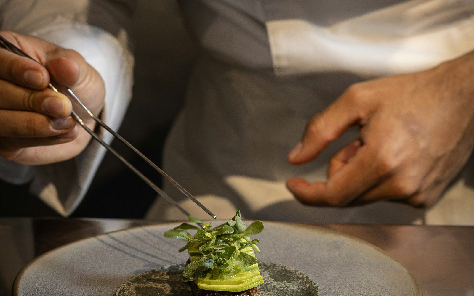 A chef plating a dish with tweezers
